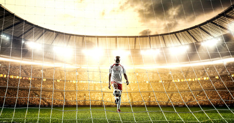 Soccer player is juggling a ball in front of the goal on the professional soccer stadium.