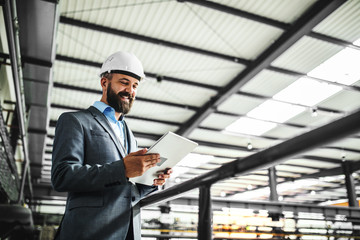 A portrait of an industrial man engineer with tablet in a factory.