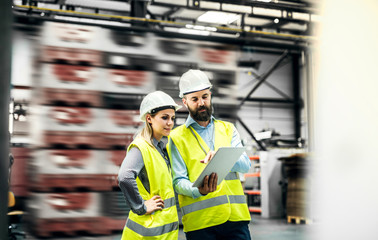 A portrait of an industrial man and woman engineer with tablet in a factory, working.