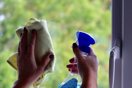 Lady cleaning a glass panel window with cloth and cleaning spray