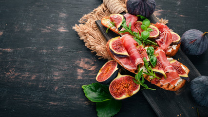 Bruschetta with prosciutto, fresh figs and cheese. On the old background. Healthy food. Free space for text. Top view. - obrazy, fototapety, plakaty