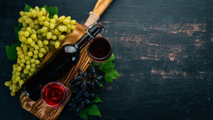 Red wine in a bottle with a glass and grapes. On a black wooden background. Free space for text. Top view.
