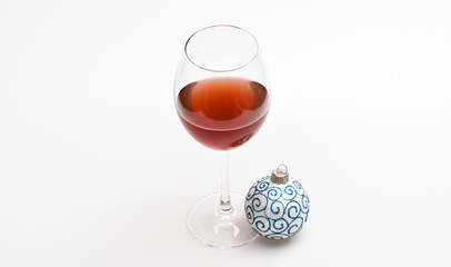 New year party concept. Wineglass with red liquid or wine and christmas ball ornament isolated on white background. Glass with wine and christmas decoration. Winter celebration with alcohol drink