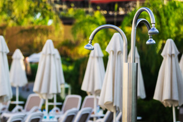 white modern deck chairs with umbrellas nearby them and a metal unusual shower standing outdoor the hotel