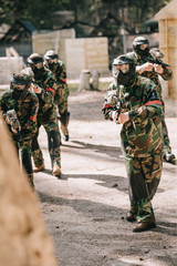 paintball team in uniform and protective masks playing paintball with marker guns outdoors