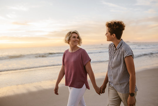 Smiling lesbian couple walking along a beach at sunset