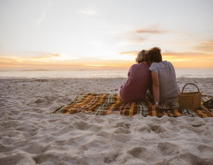 Young lesbian couple sitting on beach blanket watching the sunset