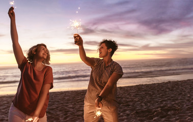 Laughing friends playing with sparklers at the beach during sunset