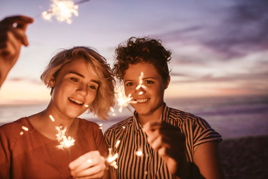 Two Friends Playing With Sparklers On The Beach At Dusk