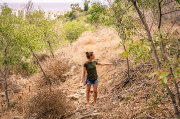 A woman in the summer walks uphill overcoming obstacles from stones and shrubs