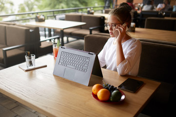 Mixed race freelancer working with convertible laptop and talking on cellphone with client in cafe....