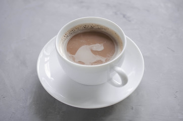 A cup of warm cocoa or chocolate on a gray table.