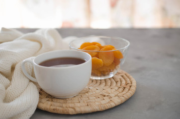 Cup of tea and dried apricots on a table, candles and knited blanket.