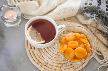 Cup of tea and dried apricots on a table, candles and knited blanket.
