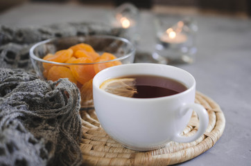 Cup of tea and dried apricots on a table, candles and knited blanket.