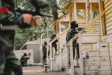 paintball team in uniform and protective masks standing on staircase of wooden towers with paintball guns outdoors