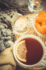 Cup of tea and dried apricots on a table, candles and knited blanket.