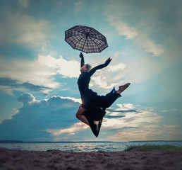Beautiful young girl in black dress with umbrella dancing by the lake