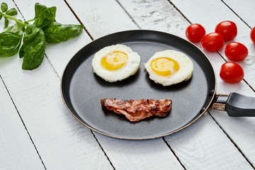 two delicious fried eggs and fried bacon arranged in a smiling face in a pan on a white kitchen table