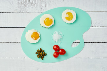 three delicious fried egg tomatoes and basil leaves on chopping board on a white wooden table