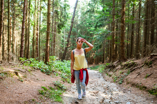 Beautiful woman smiling at path in a forest during hiking on a hill during sunrise on summer