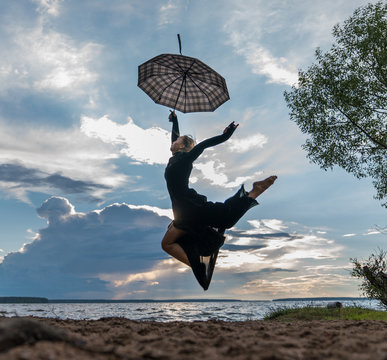 Beautiful young girl in black dress with umbrella dancing by the lake