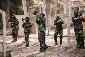 paintball team in uniform and protective masks shooting by paintball guns outdoors