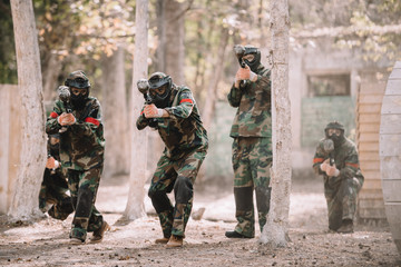 paintball team in uniform and protective masks running and aiming by paintball guns outdoors