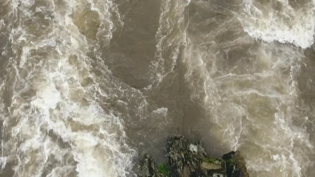 Overhead aerial of a strange shaped boulder in a turbulent river. Slow motion. The Rio Abanico on the Amazonian slopes of the Andes, Morona Santiago province, Ecuador, after heavy rain.