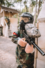 Fototapeta premium focused male paintballer in goggle mask covered by paintball splash aiming by marker gun outdoors