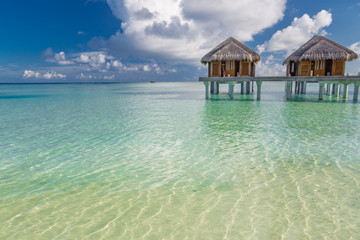 Water villas in lagoon, Maldives resort island in sunset. Detail of palm leaves on foreground. Vacation and beach relaxation, summer holidays background