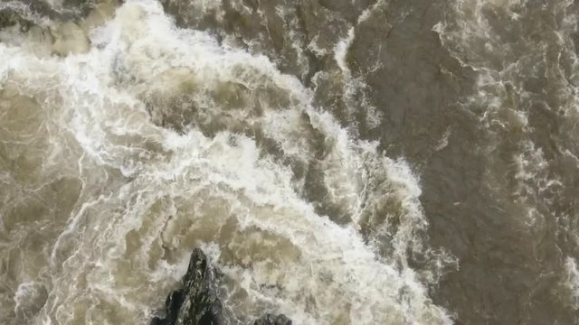 Overhead aerial of a strange shaped boulder in a turbulent river. Slow motion. The Rio Abanico on the Amazonian slopes of the Andes, Morona Santiago province, Ecuador, after heavy rain.