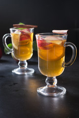Glass of tea with lemon, spiced, sliced apple and cinnamon on black board. Autumn still life.