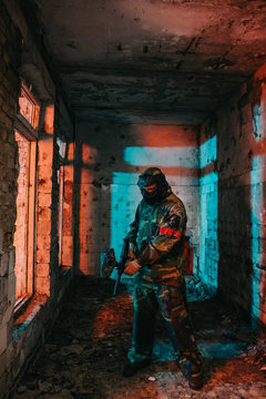 male paintball player in goggle mask and camouflage loading paintball gun in abandoned building