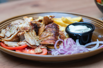 Griechisches Essen knusprige Döner Gyros Teller Portion mit Kartoffeln Pommes Frites und Zaziki Joghurt und roten zwiebeln 