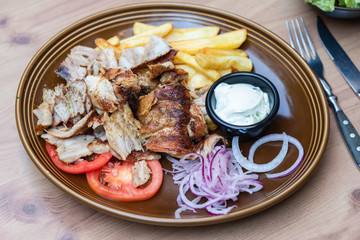 Griechisches Essen knusprige Döner Gyros Teller Portion mit Kartoffeln Pommes Frites und Zaziki Joghurt und roten zwiebeln 