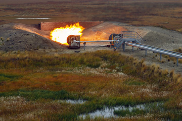 Oil, gas industry. Group wellheads and valve armature , Gas flare vertical installation, Gas  burning torch against the sunset sky,, copy space