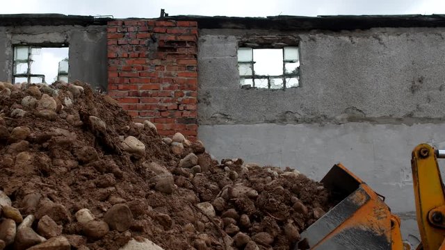 A large loader gathers stones into the ladle, a destroyed building, a close-up, loader and stones
