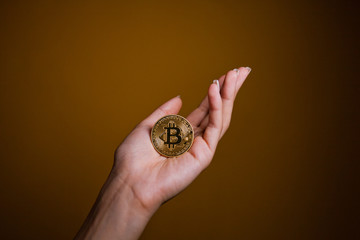 Fototapeta na wymiar Young Thin Female Hand Hold Shiny Golden Bitcoin Currency On Brown Background