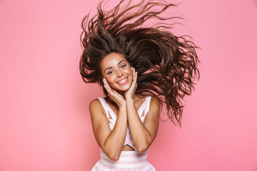 Photo of cheerful woman 20s wearing dress laughing and shaking her long brown hair, isolated over pink background