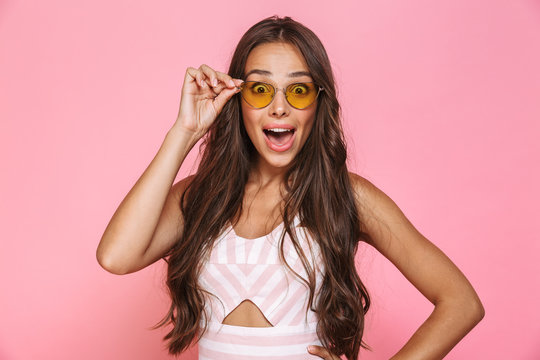 Photo of lovely woman 20s wearing sunglasses having fun and laughing, isolated over pink background