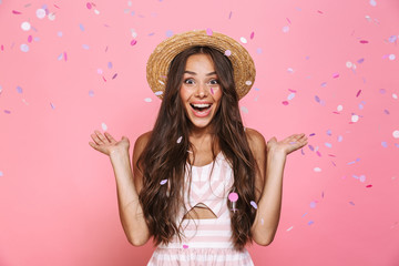 Photo of stylish woman 20s wearing straw hat laughing while standing under confetti, isolated over...