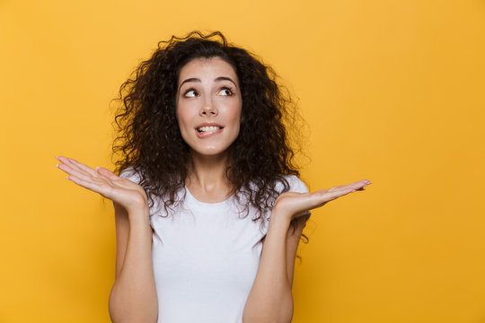 Image of cute woman 20s with curly hair laughing and throwing up hands, isolated over yellow background