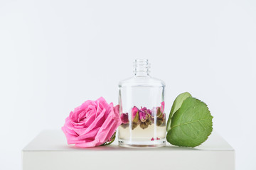 Obraz na płótnie Canvas bottle of natural herbal essential oil with roses and leaves on white cube