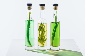 transparent bottles of essential green and yellow oils with plants on white surface