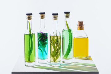 bottles of aromatic essential green and yellow oils with herbs on white cube