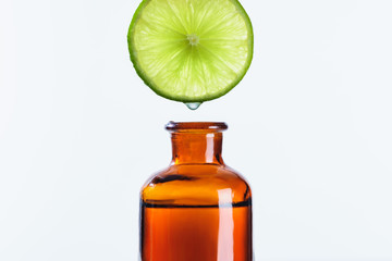 aromatic juice of lime piece dripping into bottle of natural herbal essential oil isolated on white