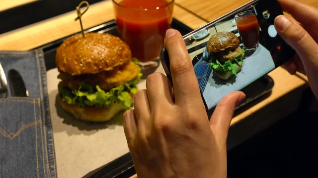 Girl makes a photo of burger and tomato juice on a smartphone in a cafe close up