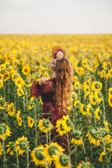 Young beautiful woman in a dress among blooming sunflowers. Agro-culture.