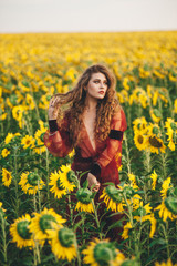 Naklejka na ściany i meble Young beautiful woman in a dress among blooming sunflowers. Agro-culture.